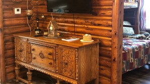 Interior de una cabaña de madera con un televisor montado en la pared, un aparador de madera y una cama con colcha.