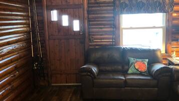 A log cabin interior with a leather sofa, a patterned rug, and a wooden door.