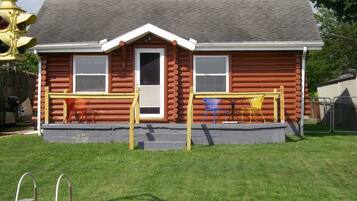 A log cabin with a front porch, two windows, and a door.