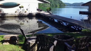 A dock extending into a calm lake, surrounded by greenery and a wooden building with outdoor seating.