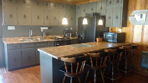 A kitchen with wooden cabinets, a granite countertop, a refrigerator, a microwave, and bar stools.