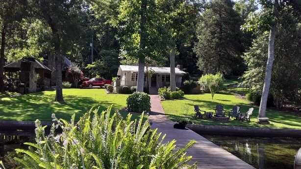 A wooden dock leading to a house with a lawn and a pond.
