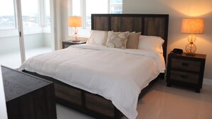 A modern bedroom with a large bed, two bedside tables with lamps, a view through a sliding door, and a nightstand with a lamp. - Beach Front Building sits on the sand/ocean<br>  Newly  remodeled  beautiful condo<br> (Fort Lauderdale)