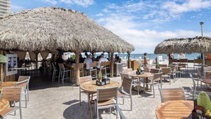 An outdoor café with thatched umbrellas, wooden tables, and chairs, overlooking the sea. - Beach Front Building sits on the sand/ocean<br>  Newly  remodeled  beautiful condo<br> (Fort Lauderdale)