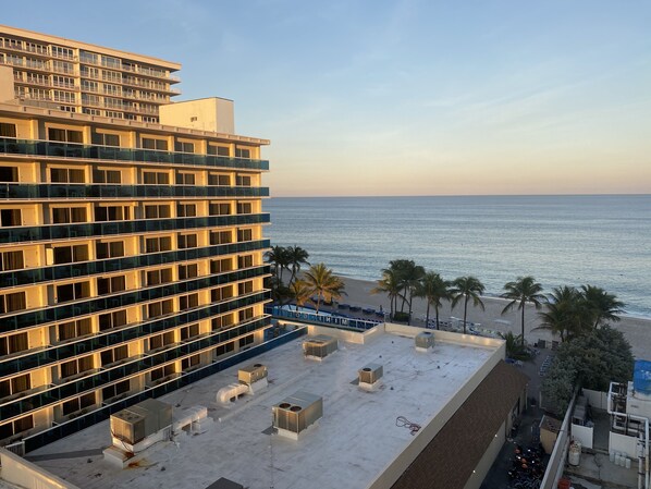 A hotel with a rooftop terrace overlooking the beach, featuring multiple balconies and air conditioning units.