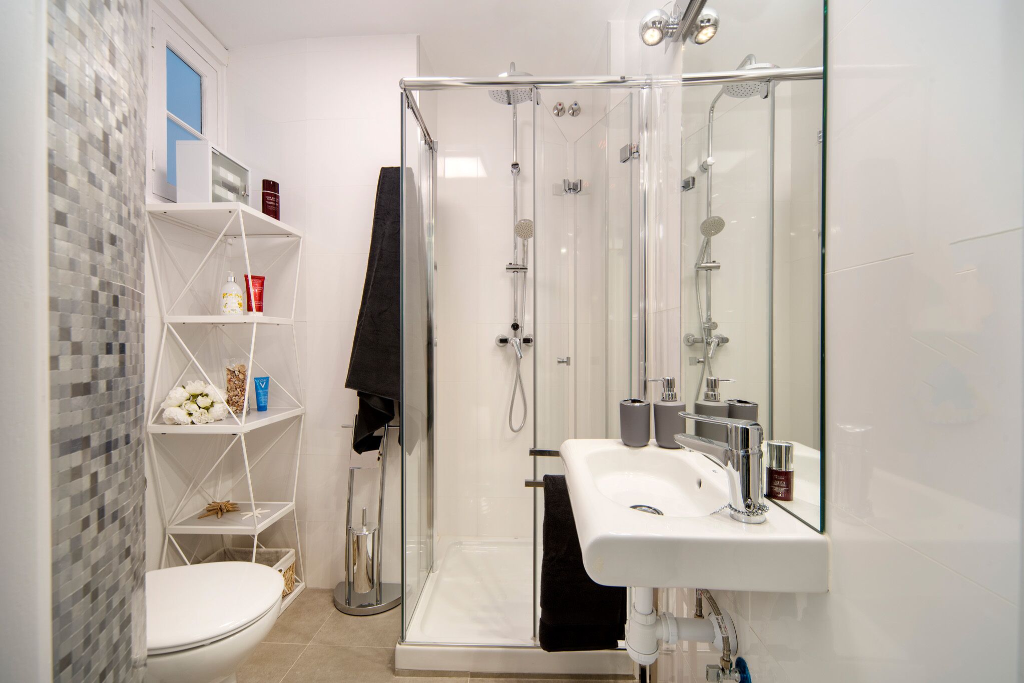 Une salle de bain moderne avec une douche à parois de verre, un lavabo blanc et une zone de douche carrelée.