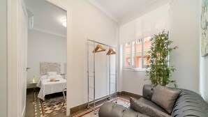 Een moderne slaapkamer met een grijze bank, een houten kapstok, een kamerbreed tapijt en uitzicht op buiten.