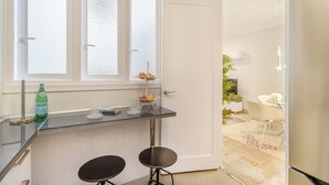Een keuken met een glazen toonbank, twee zwarte stoelen, een raam met geëtste glas en een deur naar een eetruimte.