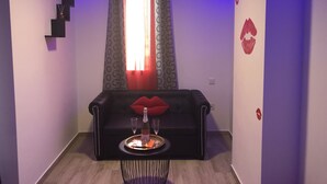Una sala de estar moderna con un sofá de cuero negro, una mesita redonda con una bandeja y una ventana con cortinas estampadas.