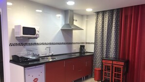 Una cocina compacta con microondas, pileta y taburetes rojos.