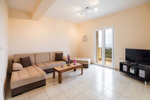 A living room with a sofa, a coffee table, a TV, and a sliding glass door to a balcony.