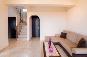 A living room with a beige sofa, a coffee table with a vase and a pink lantern, a staircase with a black railing, and a black door.