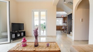 Una sala de estar con televisor, un farolillo rosa y un florero sobre una mesa. Hay una puerta corrediza de vidrio que da a un balcón.