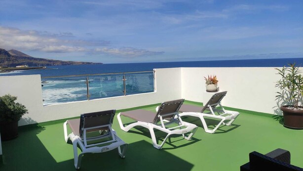 Un balcon avec deux fauteuils blancs et une petite table, d’où l’on peut admirer un plan d’eau et une côte lointaine.