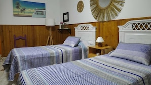 Une chambre avec deux lits, des boiseries, un tableau représentant une plage, un miroir et une lampe.