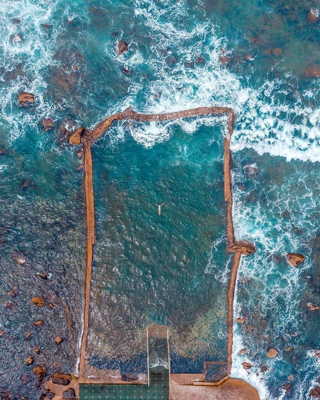 Vue aérienne d’une plage avec une zone de baignade rectangulaire entourée de vagues.