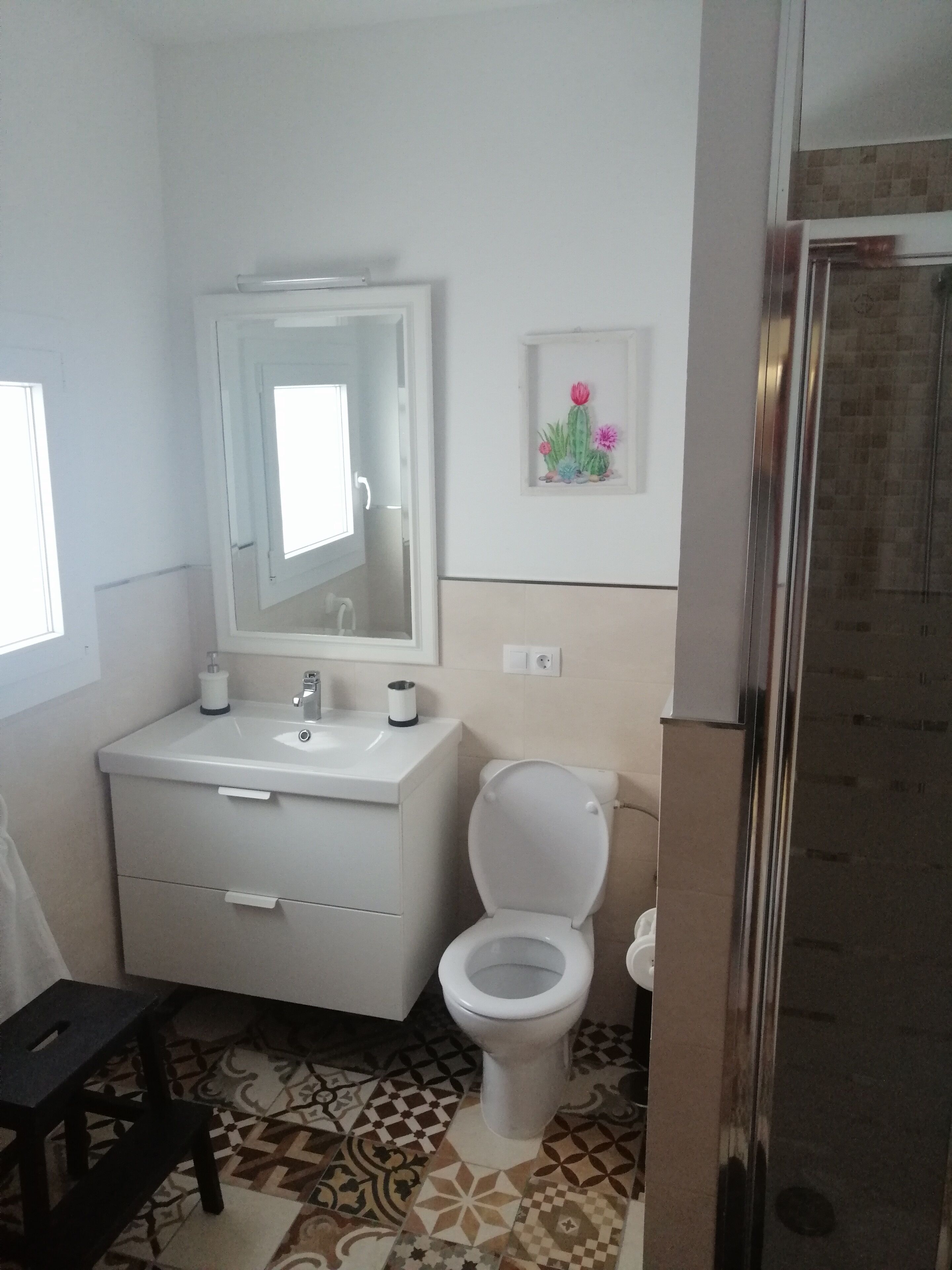 Une salle de bain avec un lavabo blanc, un miroir, des toilettes et un espace douche.