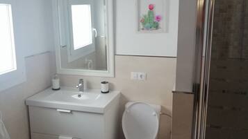 Une salle de bain avec un lavabo blanc, un miroir, des toilettes et un espace douche.
