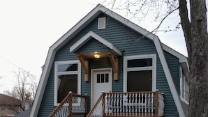 A house with a steep gable roof, a front porch with a railing, and a staircase leading to the entrance. - Kingfield, Minneapolis; Sleeps 6; New Construction, 3 Miles from Downtown (Minneapolis)