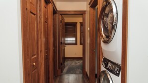 A laundry room with a front-loading washing machine, wooden doors, and a tiled floor. - Kingfield, Minneapolis; Sleeps 6; New Construction, 3 Miles from Downtown (Minneapolis)