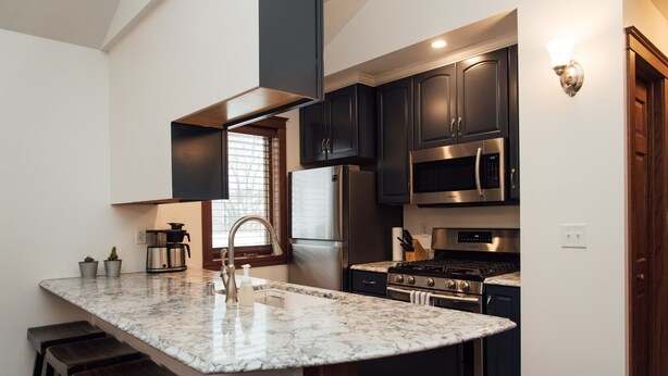 A modern kitchen with dark cabinets, stainless steel appliances, and a marble countertop. - Kingfield, Minneapolis; Sleeps 6; New Construction, 3 Miles from Downtown (Minneapolis)