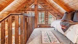 A cozy attic bedroom with a wooden sloped ceiling, a bed with pillows, and a decorative rug.