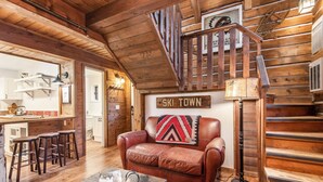 A cozy cabin interior with a leather sofa, a wooden staircase, and a sign reading "SKI TOWN".