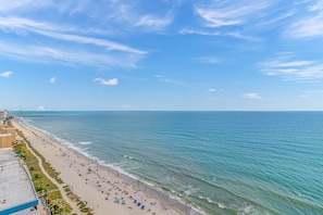 A beach with a clear sky, a long stretch of sand, and a few buildings along the shore. - The Palace 603 (Myrtle Beach)