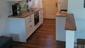 Een kleine keuken met witte kasten, een koffieapparaat en een houten aanrecht.