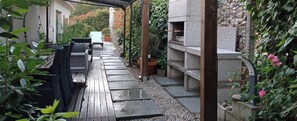 A wooden deck with a seating area, a stone structure, and a garden with plants and flowers. - House with pool of 14 m ecological (Porriño)