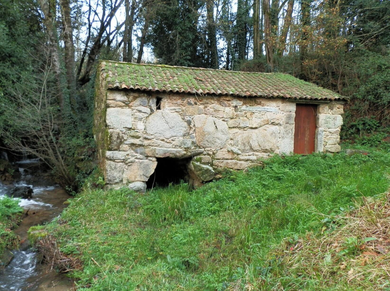 Un edificio de piedra con techo de tejas, puerta de madera y una pequeña entrada.
