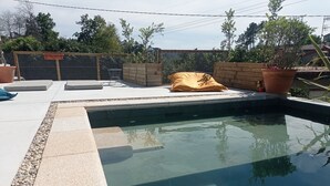 Ein Schwimmbecken mit Holzterrasse, einem gelben Kissen und einem Blumentopf.