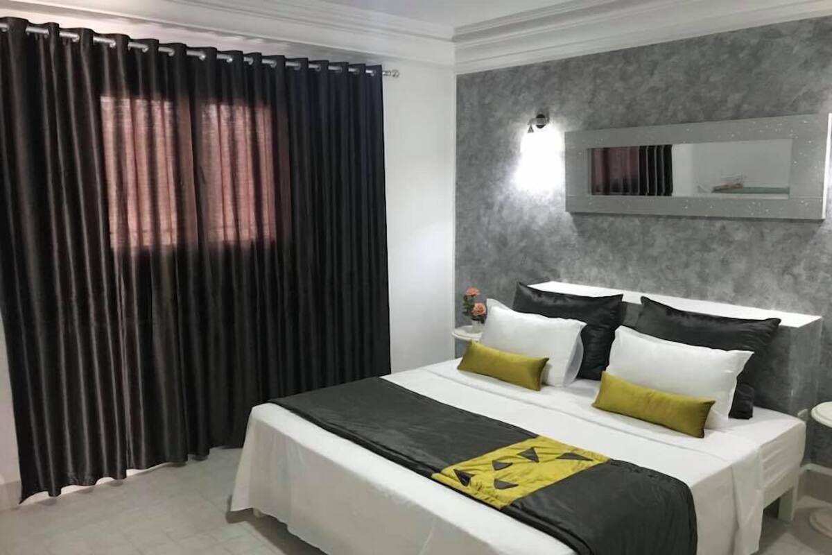 Une chambre d’hôtel avec un lit, des rideaux, une table de chevet et un miroir fixé au mur.