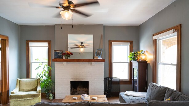 Una sala de estar con chimenea, ventilador de techo y un amplio ventanal.