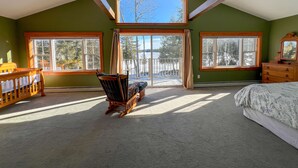 Une chambre avec une grande lucarne, donnant sur un lac, et une chaise en bois.