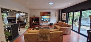 A modern living room with a sofa, a coffee table, a fireplace, and a large window with a view of the outdoors.