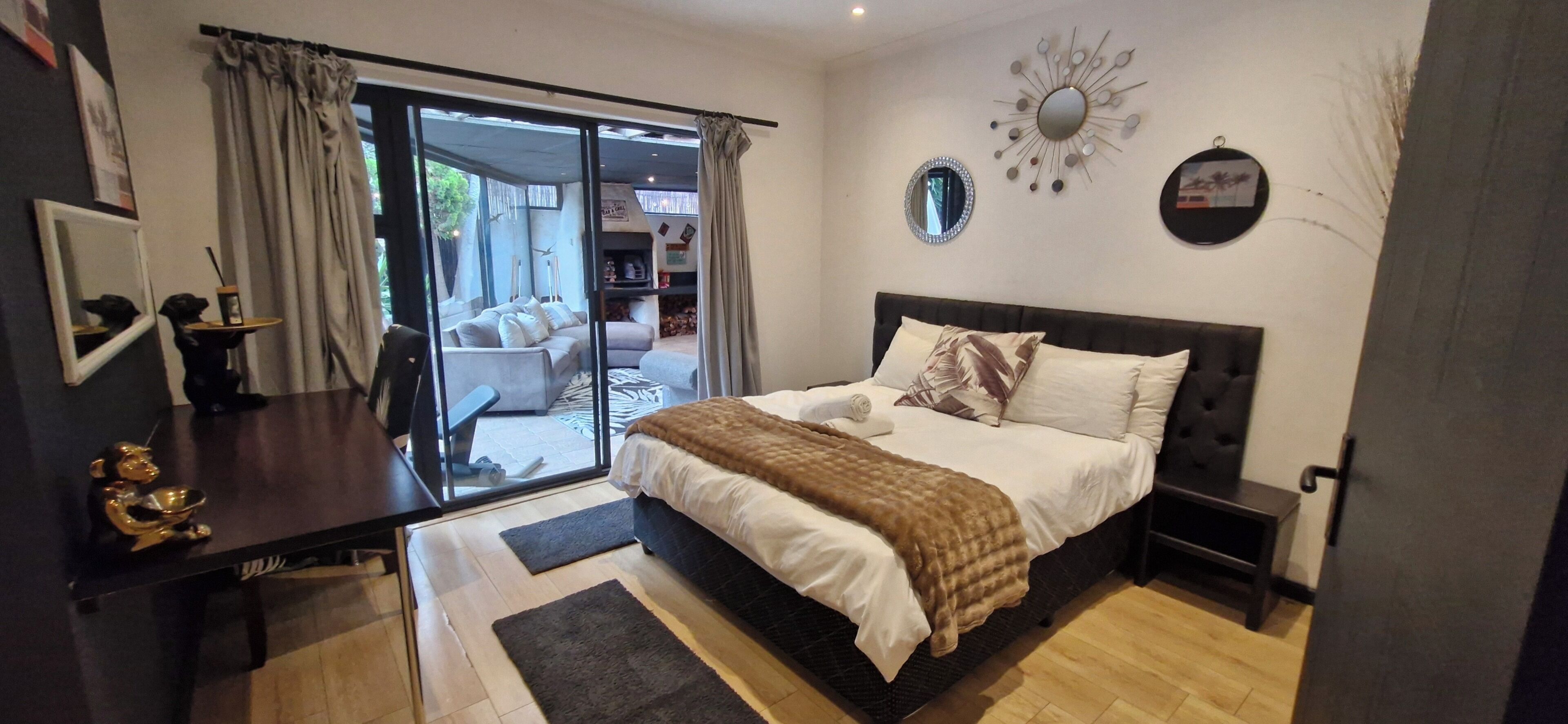 Een slaapkamer met een bed, een bureau, een stoel, een groot raam en een schuifdeur naar een balkon.