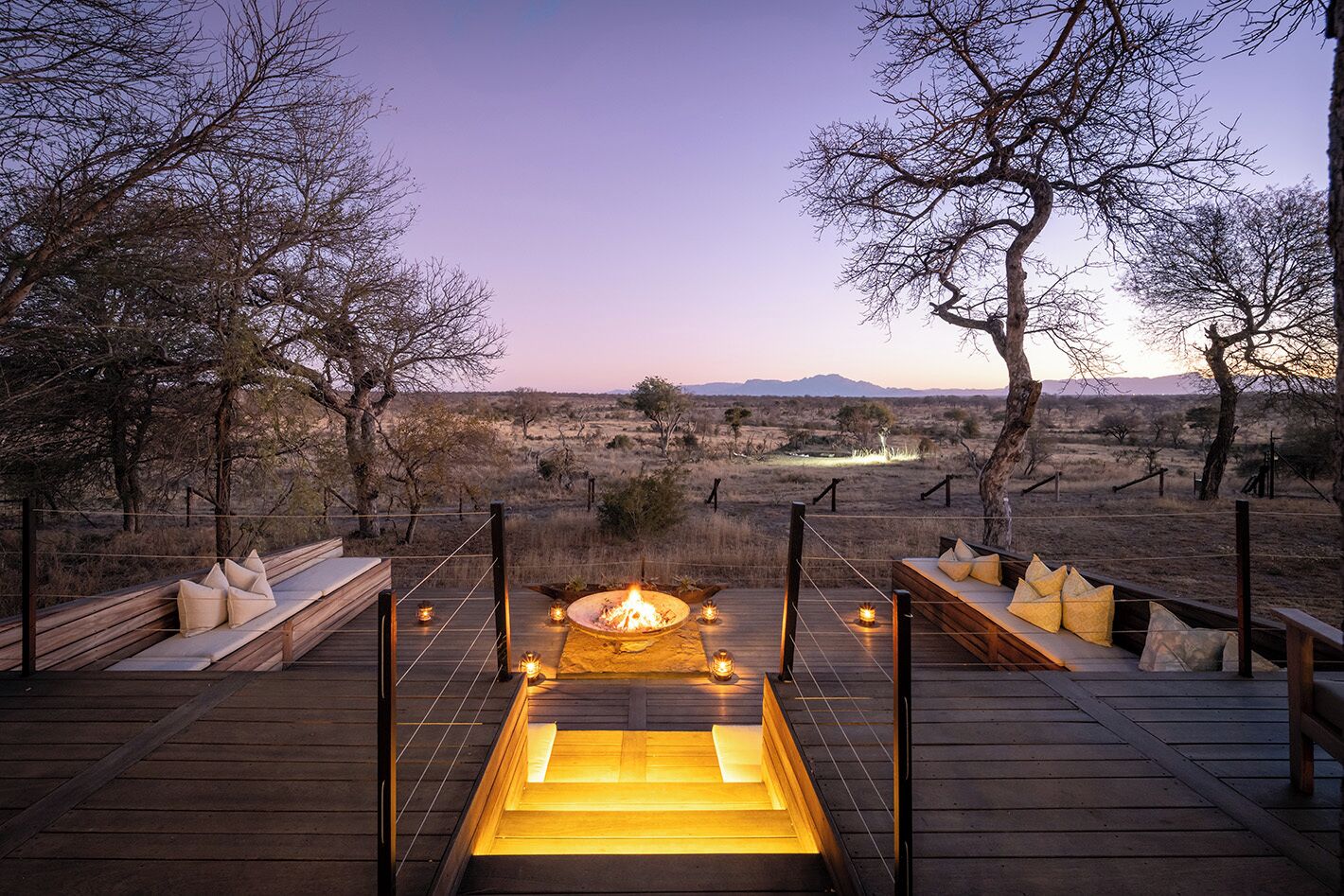 A deck with a fire pit and seating, surrounded by trees and a view of the landscape.