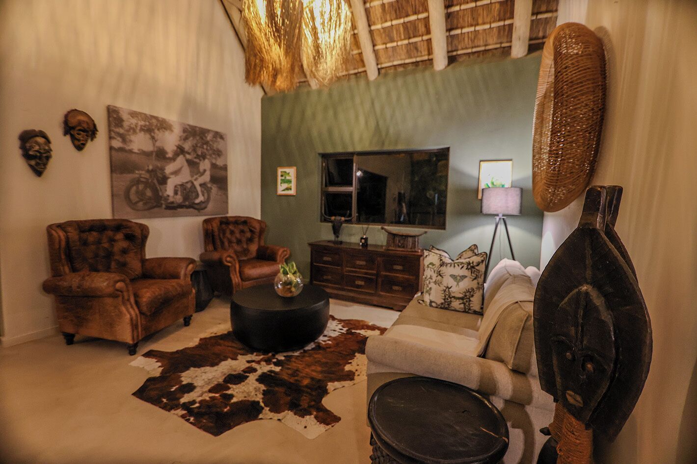 Un salón con sillones de cuero, un sofá, una mesa redonda de centro, un tapiz de cuero de vaca, un televisor y decoraciones en la pared.