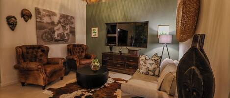 Un salón con sillones de cuero, un sofá, una mesa redonda de centro, un tapiz de cuero de vaca, un televisor y decoraciones en la pared.
