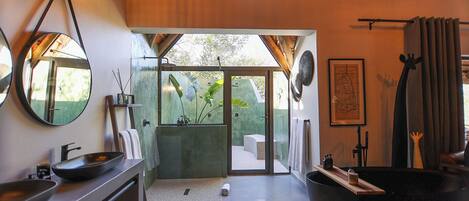 Un baño moderno con una bañera negra grande, un espejo redondo y una zona de ducha con mampara de vidrio.