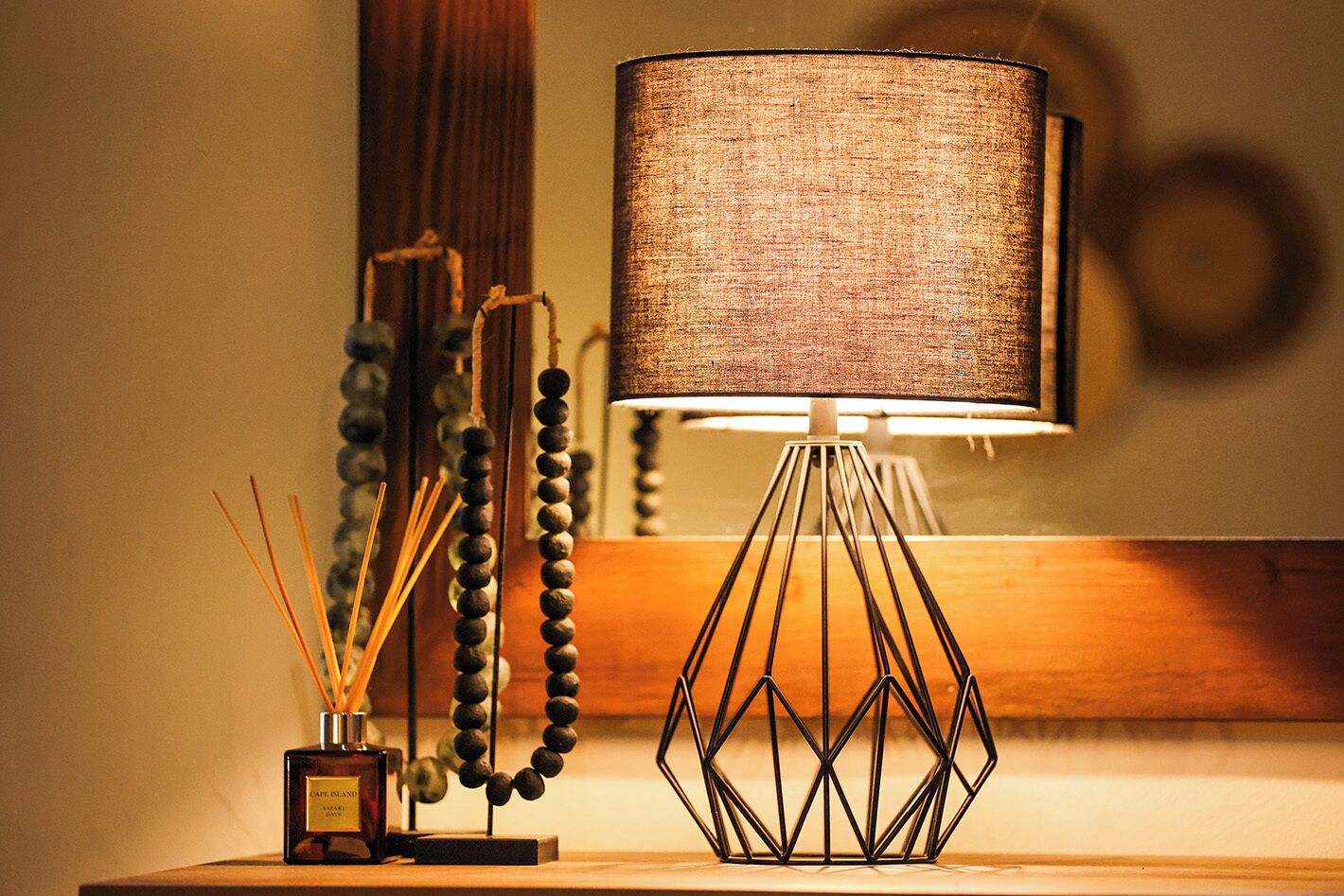 A table lamp with a geometric base and a textured lampshade, a bottle of perfume, and a decorative string of beads.