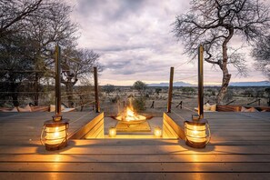 A wooden deck with a central fire feature and lanterns, surrounded by trees and a view of the landscape. - Tomo Safari Lodge (Hoedspruit)