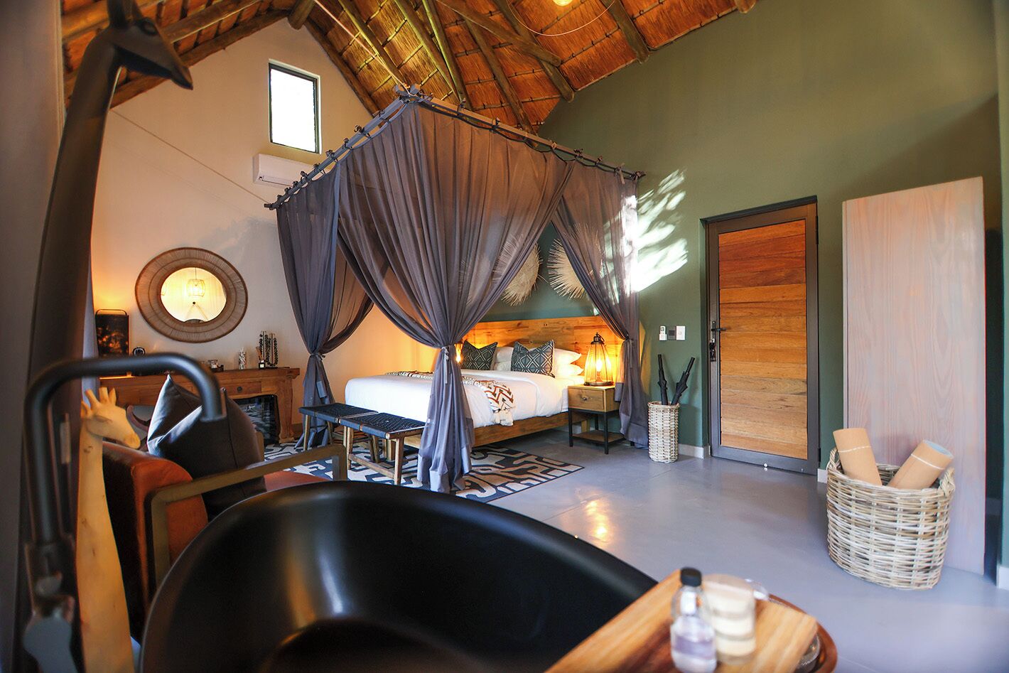 A bedroom with a canopy bed, a desk, a chair, a lamp, and a wicker basket.