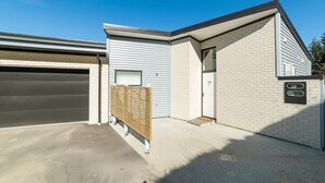 A modern two-story house with a garage, a wooden fence, and a brick exterior. - Modern One Bedroom Apartment with Lake View (Queenstown)