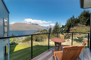 Un balcon avec une table et une chaise en bois, donnant sur un lac et des montagnes.