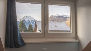 A window with a view of snow-capped mountains and a building with a sloped roof.