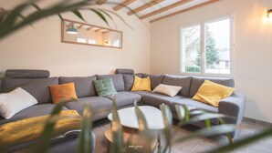 A modern living room with a grey sectional sofa, a round coffee table, and a large window providing natural light.