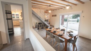 A dining area with a wooden table set for four, a staircase leading to an upper level, and a view of the outside through a glass door.