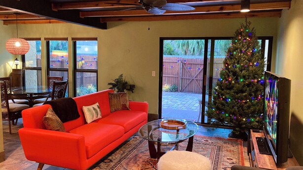 A living room with a red sofa, a glass coffee table, a white furry ottoman, and a Christmas tree with lights. - The Polynesian- 2 miles to Siesta Beach, Heated Pool, Furry Friends Stay Free (Sarasota)